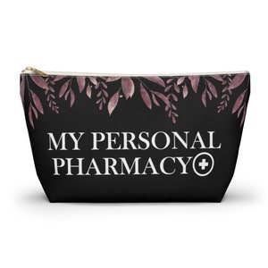 Può includere: Borsa nera con cerniera con un motivo floreale e il testo "MY PERSONAL PHARMACY+" in bianco.