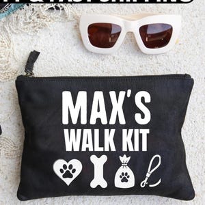 May include: Black zippered pouch with the text "MAX'S WALK KIT" in white. The pouch has a heart with paw prints, a bone, a bag with paw prints, and a leash icon. White sunglasses are above the pouch.