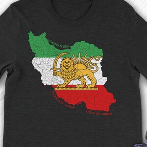 Puede incluir: Camiseta negra con un mapa de Irán y su emblema nacional, un león con una espada. El mapa está en los colores de la bandera iraní: verde, blanco y rojo. El texto "Persian Gulf" y "Gulf of Oman" es visible.