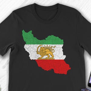 Puede incluir: Camiseta negra con un mapa de Irán en los colores de la bandera iraní: verde, blanco y rojo. La camiseta tiene un emblema de león y sol. La palabra "Black" está impresa en la parte inferior. Se ve un teléfono con el logotipo de Etsy.