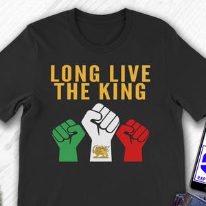 Puede incluir: Camiseta negra con el texto dorado "LONG LIVE THE KING". Debajo, tres puños en verde, blanco y rojo, con un emblema dorado en el puño blanco. Se ve un teléfono con el logo de Etsy.