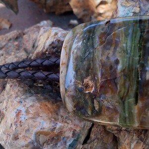May include: A brown leather bolo tie with a large, rectangular, multi-colored agate stone pendant. The stone has shades of brown, green, and white.