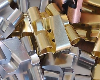 May include: A collection of metal clips in various colors, including silver, gold, and copper. The clips have a unique shape with a curved design and are likely used for fastening or holding items together. The image is a close-up shot.