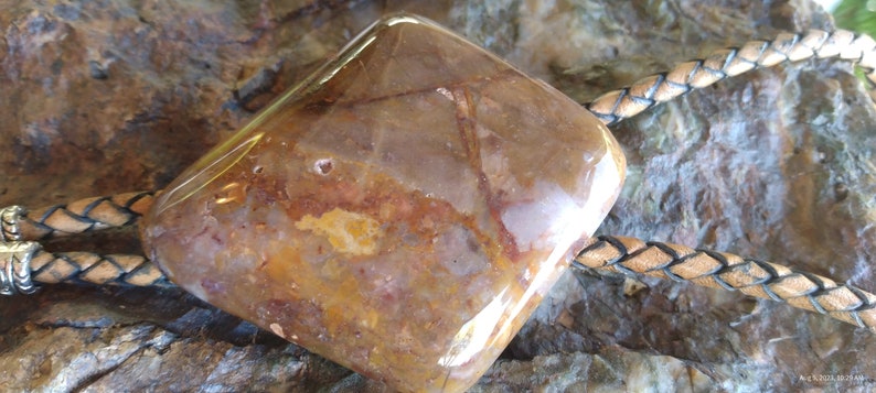 May include: A brown and white agate stone bolo tie with a leather cord. The stone is polished and has a smooth surface.