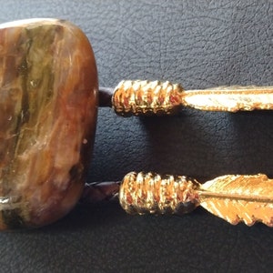 May include: A bolo tie with a large, multi-colored, agate-like stone and two gold-colored feathers.