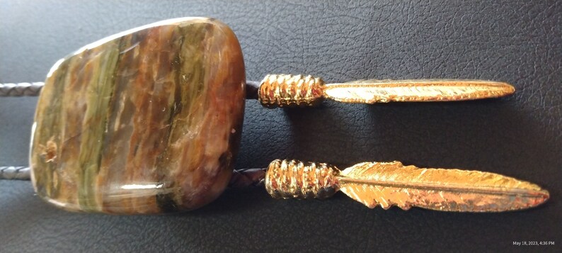 May include: A bolo tie with a large, multi-colored, agate-like stone and two gold-colored feathers.