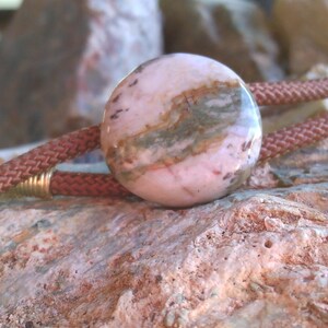 May include: A pink and brown patterned stone bolo tie with a brown leather cord.