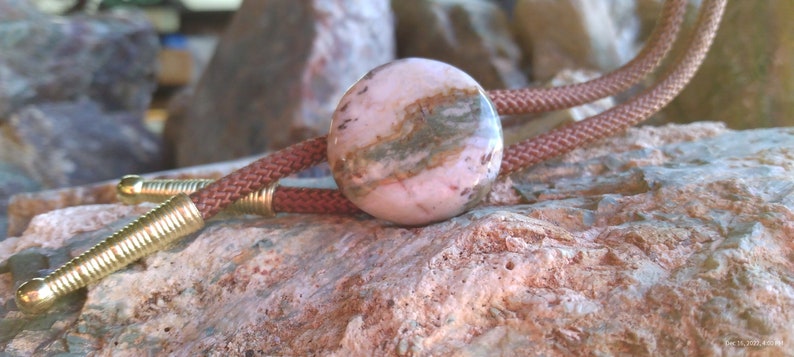 May include: A pink and brown patterned stone bolo tie with a brown leather cord.