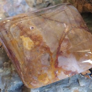 May include: A square-shaped pendant made of clear quartz with brown and white inclusions. The pendant is attached to a brown leather cord.