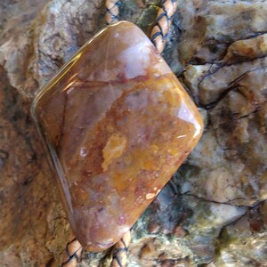 May include: A brown and orange stone bolo tie with a leather cord. The stone is a diamond shape and has a polished finish.