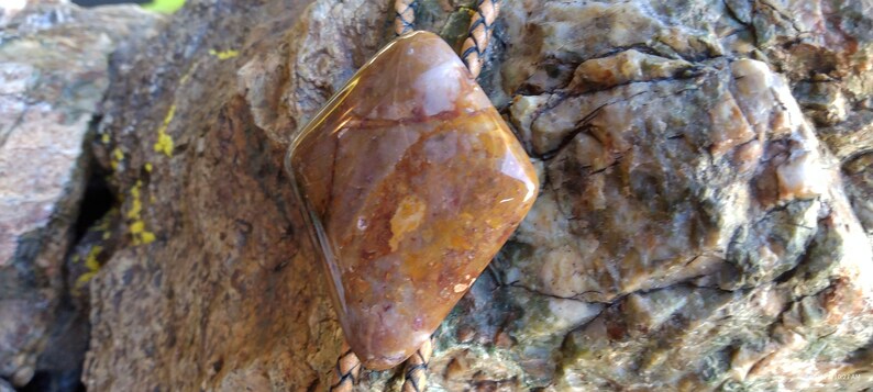 May include: A brown and orange stone bolo tie with a leather cord. The stone is a diamond shape and has a polished finish.