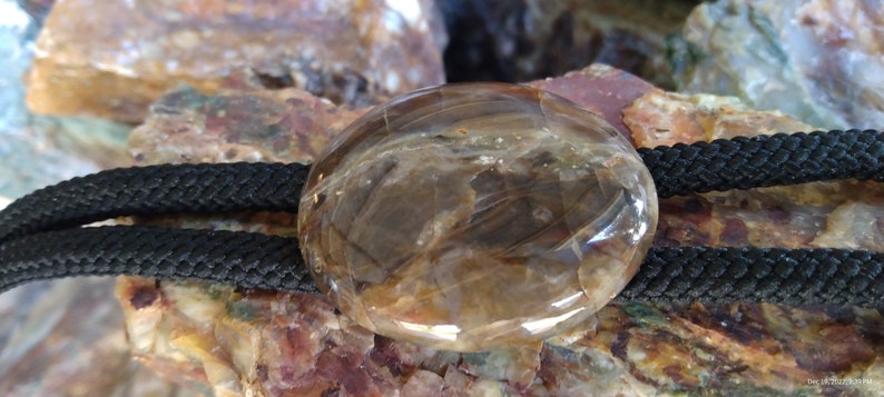 Pu&ograve; includere: Un bolo tie in agata marrone e trasparente con un cordoncino nero. L'agata &egrave; lucidata e presenta un motivo naturale.