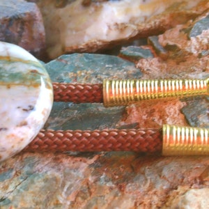 May include: A bolo tie with a round, multi-colored agate stone pendant and brown braided cord with gold metal tips.