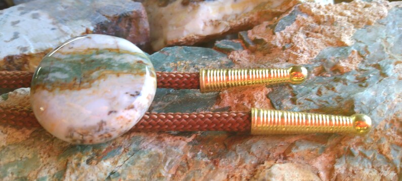 May include: A bolo tie with a round, multi-colored agate stone pendant and brown braided cord with gold metal tips.