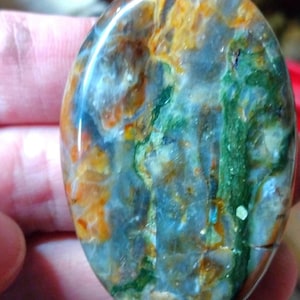 Può includere: Un bolo tie con un grande ciondolo ovale in pietra. La pietra è un mix di colori blu, verde, arancio e bianco. Il bolo tie è fatto di pelle marrone.