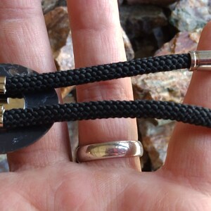 Pu&ograve; includere: Un bolo tie nero con uno slider rotondo in metallo nero e due punte a proiettile argentate.