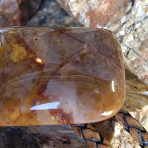 May include: A square-shaped, translucent, brown and white agate stone with a polished surface. The stone is set in a leather cord.
