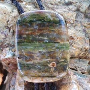 May include: A green, brown, and white agate bolo tie with a polished, rectangular stone.