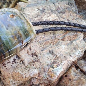 May include: A bolo tie with a large, multi-colored agate stone as the centerpiece. The stone has shades of brown, green, and blue. The bolo tie cord is black leather.
