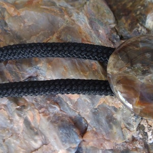 Pu&ograve; includere: Un cravattino bolo con un cordoncino nero e punte a proiettile argentate. Il cravattino bolo presenta una pietra rotonda, marrone, simile all'agata con un motivo a spirale.