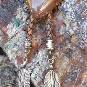 May include: A brown leather bolo tie with a large, clear, brown and yellow agate stone pendant. The tie has silver feather charms hanging from the ends.