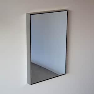 Peut inclure: Un miroir rectangulaire avec un cadre gris et un bord noir est monté sur un mur blanc. Le miroir reflète un coin de pièce avec un sol gris et des murs blancs. Le miroir est de conception simple et moderne.