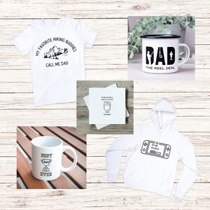 Op de afbeelding: Een set vaderdagcadeaus met een wit T-shirt met de tekst "My Favorite Hiking Buddies Call Me Dad", een witte mok met de tekst "Best Dad Ever" en een trofee-afbeelding, een witte hoodie met een videogamecontroller-afbeelding, een witte kaart met de tekst "No one can hold a candle to you Dad You're Flammable!" en een witte emaille mok met de tekst "Dad The Reel Deal" en een visafbeelding.