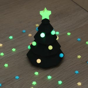 Könnte beinhalten: Ein schwarzer, kegelförmiger Weihnachtsbaumschmuck mit mehreren Ebenen, gekrönt von einem leuchtenden lindgrünen Stern. Der Baum ist mit integrierten, leuchtenden Kugellichtern in Blau, Gelb und Grün versehen, umgeben von kleinen Sternkonfetti.