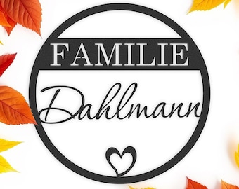 Könnte beinhalten: Schwarzes rundes Schild aus Metall mit dem Text "FAMILIE Dahlmann" und einem kleinen Herz in der Mitte. Das Schild ist von Herbstblättern in Orange- und Gelbtönen umgeben.