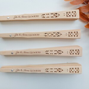 May include: Four wooden hand fans with intricate cutouts and the text "Dia & Aaron 08.04.2029" engraved on each.