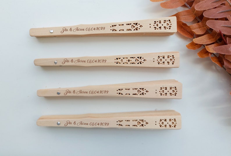 May include: Four wooden hand fans with intricate cutouts and the text "Dia & Aaron 08.04.2029" engraved on each.