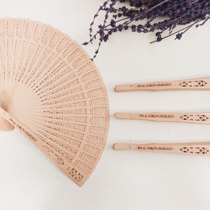 May include: Four wooden hand fans with a decorative cut-out design. The fans are personalised with the text "PIA & AARON 05.08.2013".