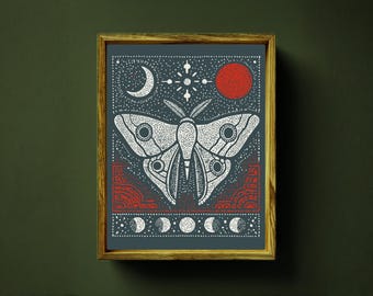 May include: Framed art print featuring a detailed illustration of a moth with celestial elements. The artwork is in white and red on a dark blue background, with a crescent moon, sun, and phases of the moon. The frame is made of wood.