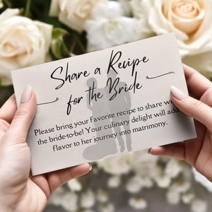 May include: A beige recipe card held by hands, with the text "Share a Recipe for the Bride." The card includes a silhouette of a couple and invites guests to share recipes for the bride-to-be, adding flavor to her journey.