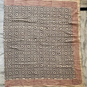 May include: A cream-colored cotton fabric with a black and white floral pattern. The fabric has a red border with a geometric design.