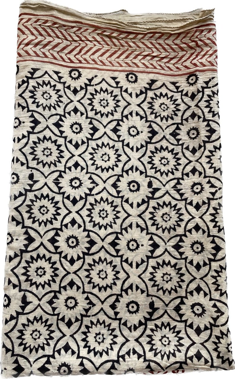 May include: A white cotton fabric with a black and red block print pattern. The fabric has a geometric design with a repeating pattern of flowers.