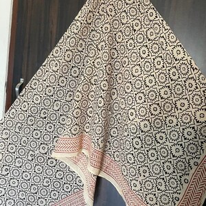 May include: A cream-colored cotton scarf with a black floral pattern and a red border. The scarf is folded and hanging on a hook.
