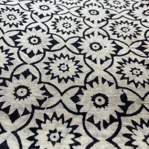 May include: Black and white fabric with a repeating geometric pattern of stylized flowers. The fabric has a slightly textured surface.