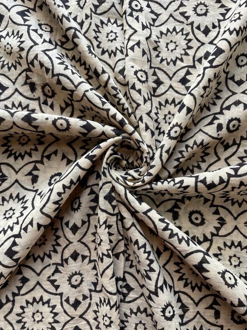 May include: A beige fabric with a black and white geometric pattern. The fabric is folded and has a soft, textured feel.
