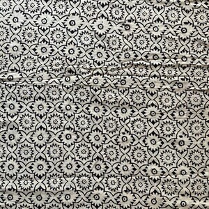 May include: Black and white fabric with a repeating pattern of stylized flowers. The fabric has a textured surface.