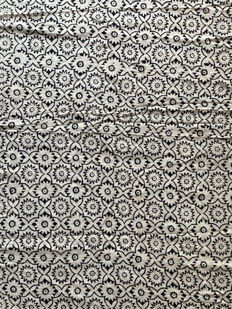 May include: Black and white fabric with a repeating pattern of stylized flowers. The fabric has a textured surface.