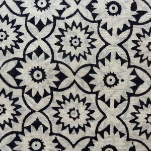 May include: Black and white fabric with a repeating pattern of stylized flowers. The flowers have a central circle and radiating points.