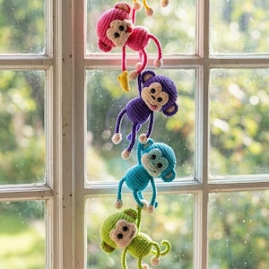 May include: A vertical chain of six crocheted monkeys in bright colors including yellow, pink, purple, blue, green, and light purple. Each monkey features a cream-colored face, black eyes, and small limbs, linked together in a hanging display.