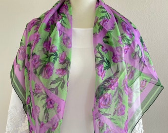 May include: A light purple and green floral patterned scarf with a black trim. The scarf is made of a sheer fabric and has a delicate floral design.