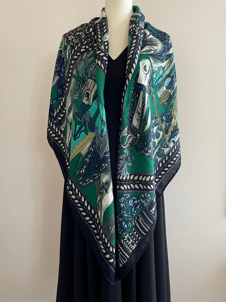 Peut inclure: Un foulard carr&eacute; en soie avec un motif &eacute;questre d&eacute;taill&eacute;. Le foulard pr&eacute;sente un fond vert fonc&eacute; avec des illustrations de chevaux, de cavaliers et d'&eacute;l&eacute;ments floraux en bleu, sarcelle et blanc. La bordure est bleu marine fonc&eacute;.