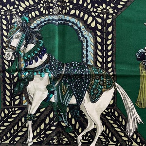 Peut inclure: Un foulard en soie vert avec une illustration d&eacute;taill&eacute;e d'un cheval blanc orn&eacute; d'une sellerie orn&eacute;e. Le cheval est plac&eacute; sur un fond d'arcades d&eacute;coratives et de feuillage dans des tons de vert, de bleu et de noir.