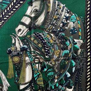 Peut inclure: Foulard carr&eacute; en soie repr&eacute;sentant deux chevaux blancs orn&eacute;s d'une sellerie color&eacute;e et de perles. Les chevaux se d&eacute;tachent sur un fond vert fonc&eacute; avec une bordure d&eacute;corative dans les tons de turquoise, marine et cr&egrave;me.