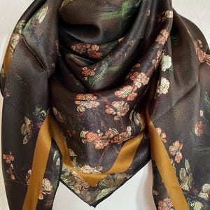 May include: A black silk scarf with a floral print and a gold border. The flowers are in shades of red, orange, and green.