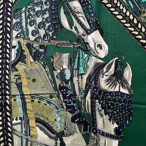 Peut inclure: Un carr&eacute; de soie avec un motif &eacute;questre d&eacute;taill&eacute;. L'&eacute;charpe pr&eacute;sente deux chevaux blancs avec des harnachements et des brides orn&eacute;s, sur un fond vert fonc&eacute;. Le motif comprend des &eacute;l&eacute;ments d&eacute;coratifs dans les tons de bleu, d'or et de vert.