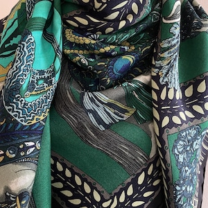 Peut inclure: Un foulard carr&eacute; &agrave; motifs dans les tons de turquoise, vert, marine et cr&egrave;me. Le foulard pr&eacute;sente des motifs complexes, notamment des plumes stylis&eacute;es et des motifs floraux. Les bords sont bord&eacute;s d'une bordure vert fonc&eacute; et marine.